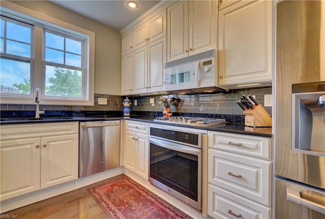 kitchen with appliances with stainless steel finishes, backsplash, sink, dark stone countertops, and hardwood / wood-style floors