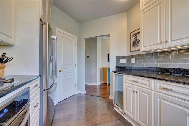 kitchen featuring stainless steel appliances, tasteful backsplash, dark stone counters, wood-type flooring, and white cabinets