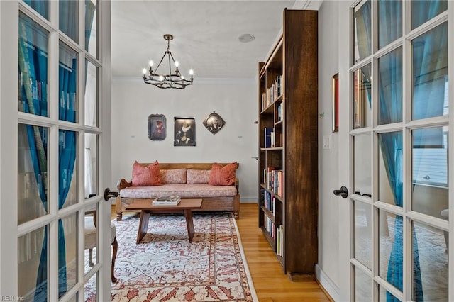 living area with french doors, an inviting chandelier, light hardwood / wood-style flooring, and ornamental molding