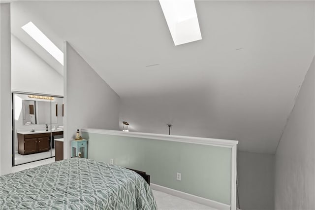 carpeted bedroom featuring vaulted ceiling with skylight and connected bathroom