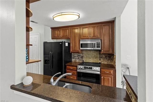 kitchen with dark stone counters, sink, decorative backsplash, appliances with stainless steel finishes, and kitchen peninsula