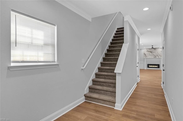 stairs featuring a premium fireplace, crown molding, and wood-type flooring