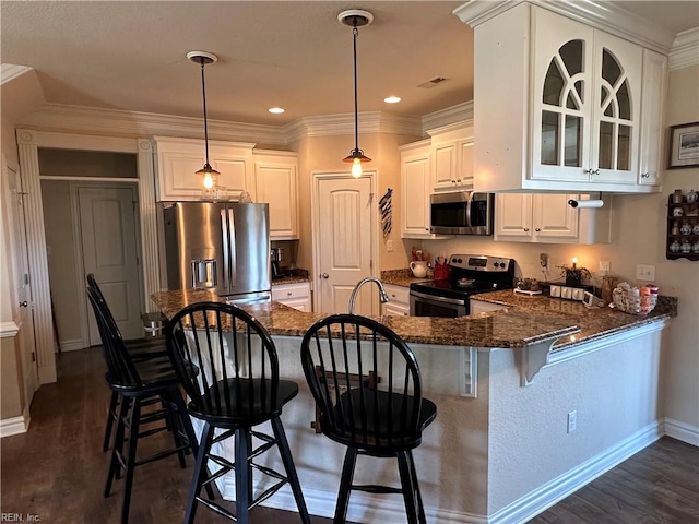 kitchen featuring white cabinets, hanging light fixtures, appliances with stainless steel finishes, dark hardwood / wood-style flooring, and kitchen peninsula