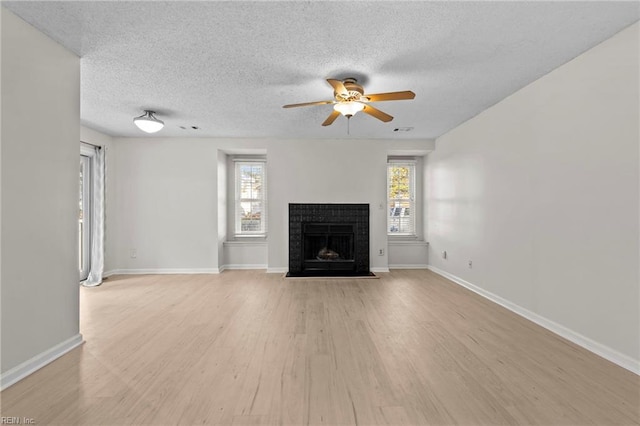 unfurnished living room featuring a fireplace, a textured ceiling, light wood-type flooring, and ceiling fan