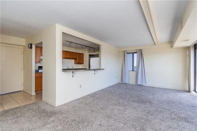 unfurnished living room with a textured ceiling, track lighting, a wealth of natural light, and light colored carpet