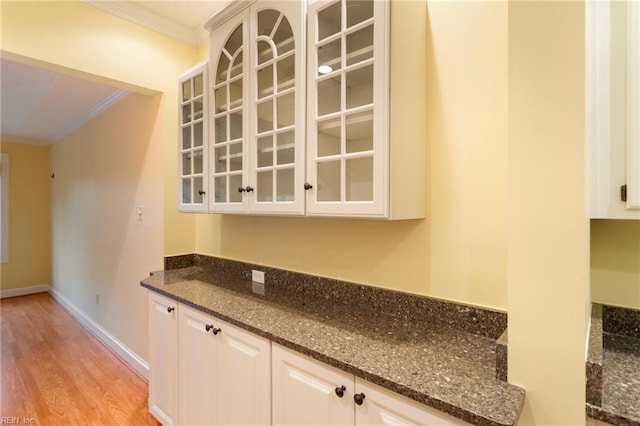 bar featuring light wood-type flooring, white cabinetry, crown molding, and dark stone countertops