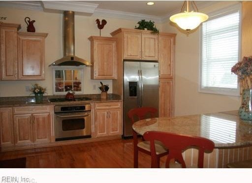 kitchen with hanging light fixtures, wall chimney exhaust hood, dark hardwood / wood-style floors, ornamental molding, and stainless steel appliances