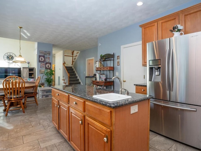 kitchen with sink, stainless steel fridge with ice dispenser, dark stone countertops, decorative light fixtures, and a kitchen island with sink