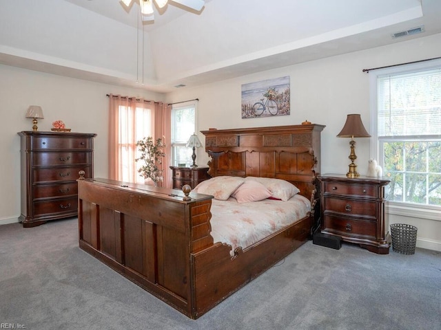 carpeted bedroom with a tray ceiling, multiple windows, and ceiling fan