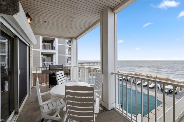 balcony with a water view, a beach view, and grilling area