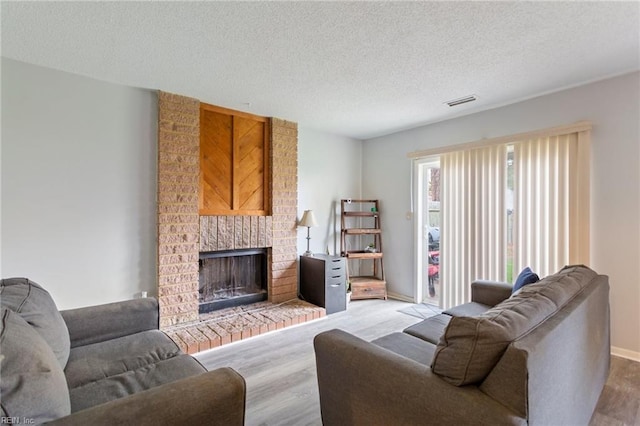 living room featuring a brick fireplace, a textured ceiling, and light hardwood / wood-style flooring