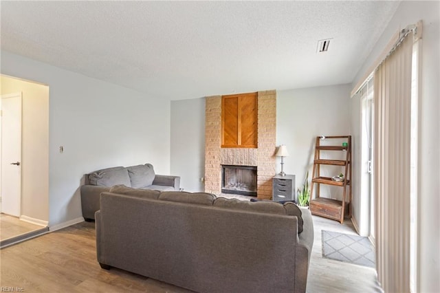 living room featuring light hardwood / wood-style floors, a textured ceiling, and a brick fireplace