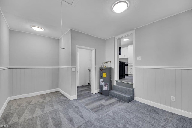 basement featuring electric water heater, wooden walls, and light colored carpet