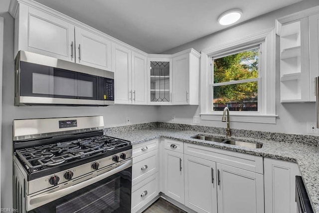 kitchen featuring light stone countertops, white cabinetry, sink, stainless steel appliances, and hardwood / wood-style floors