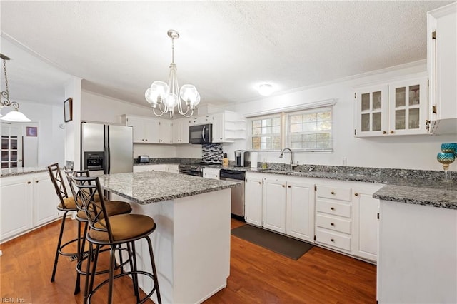 kitchen with white cabinets, decorative light fixtures, a center island, and appliances with stainless steel finishes