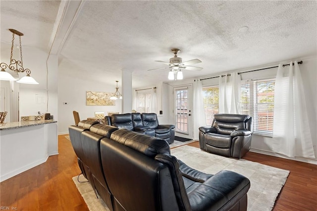 living room with ceiling fan with notable chandelier, wood-type flooring, and a textured ceiling