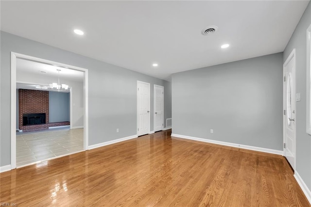 unfurnished room with a fireplace, light hardwood / wood-style floors, and an inviting chandelier