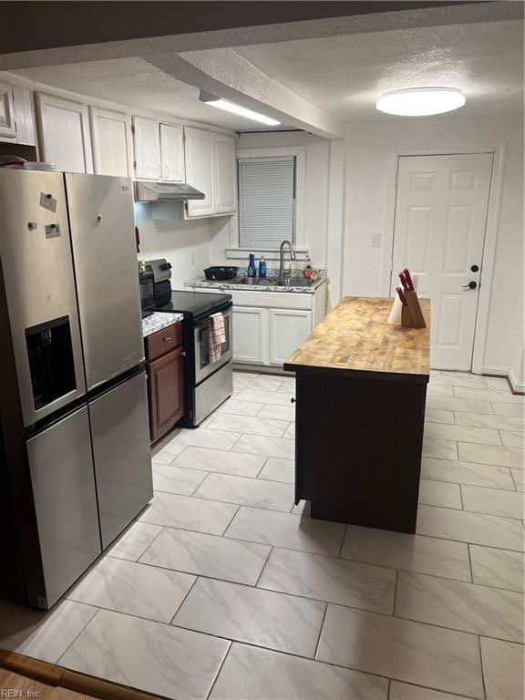 kitchen featuring a textured ceiling, under cabinet range hood, stainless steel appliances, butcher block counters, and a sink