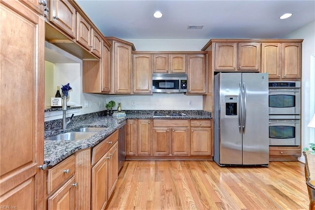 kitchen featuring dark stone counters, light hardwood / wood-style flooring, stainless steel appliances, and sink