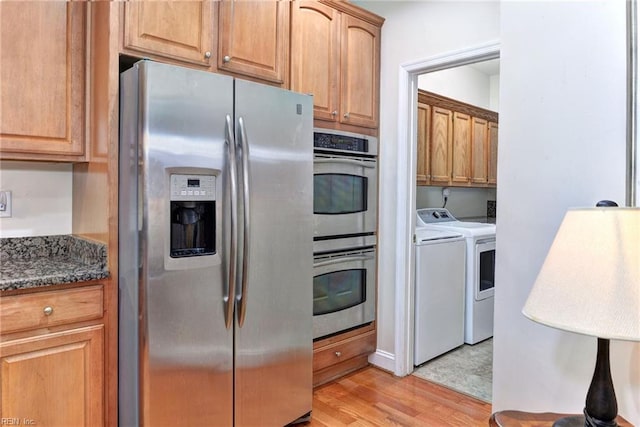 kitchen featuring stainless steel appliances, washer and clothes dryer, light hardwood / wood-style floors, and dark stone countertops