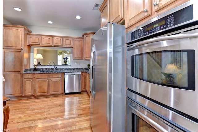 kitchen featuring dark stone countertops, sink, light wood-type flooring, and stainless steel appliances