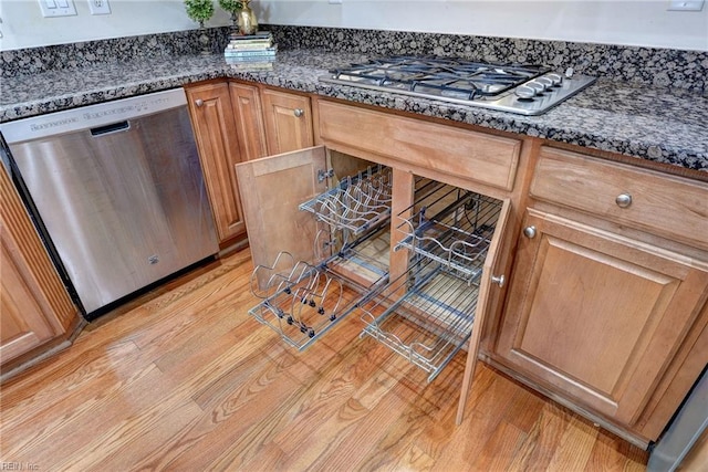 kitchen with appliances with stainless steel finishes, light wood-type flooring, and dark stone counters