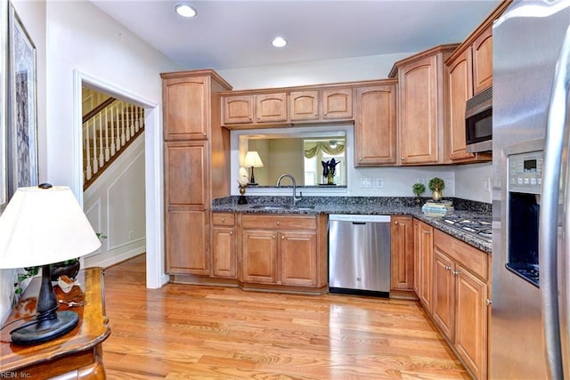 kitchen featuring dark stone countertops, light hardwood / wood-style floors, sink, and stainless steel appliances