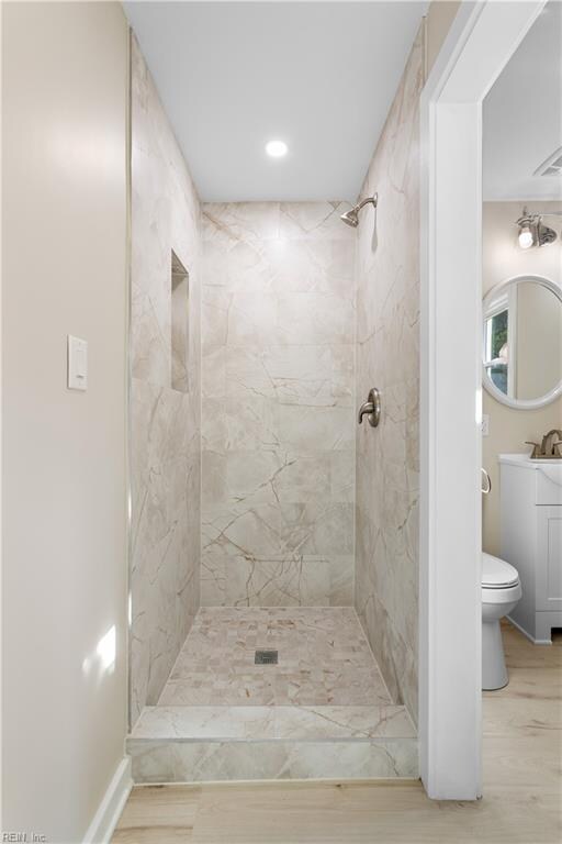 bathroom with tiled shower, vanity, hardwood / wood-style flooring, and toilet