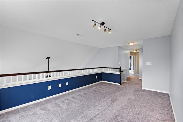 carpeted empty room with rail lighting and lofted ceiling