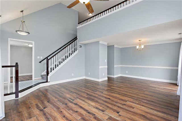 unfurnished living room featuring ornamental molding, ceiling fan with notable chandelier, high vaulted ceiling, and dark wood-type flooring