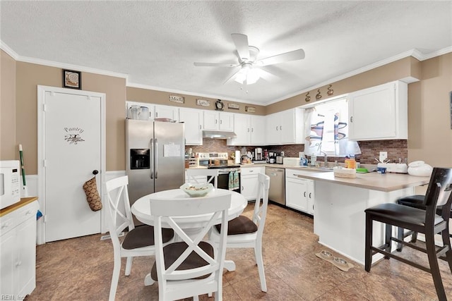 kitchen with white cabinetry, a kitchen breakfast bar, a textured ceiling, appliances with stainless steel finishes, and ornamental molding