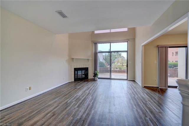 unfurnished living room featuring plenty of natural light, dark hardwood / wood-style floors, and a tiled fireplace