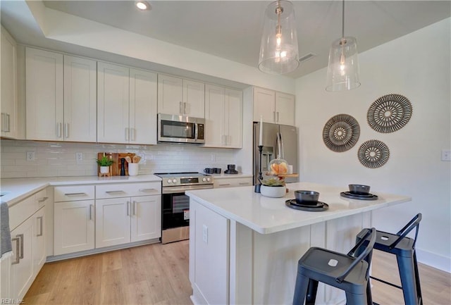 kitchen with white cabinetry, stainless steel appliances, light hardwood / wood-style floors, a breakfast bar area, and decorative backsplash