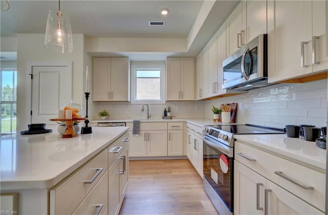 kitchen featuring decorative backsplash, pendant lighting, light wood-type flooring, and appliances with stainless steel finishes