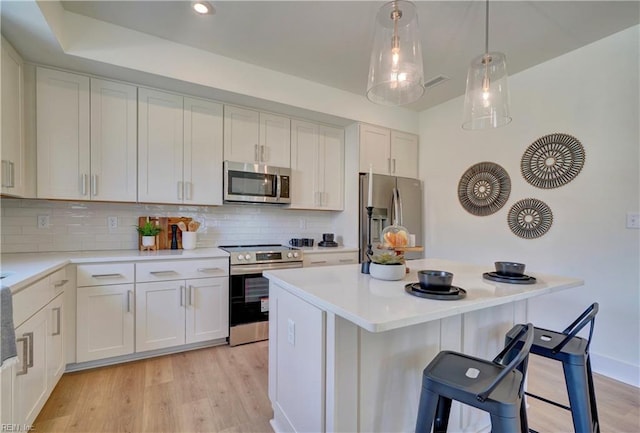 kitchen featuring decorative backsplash, light wood-type flooring, appliances with stainless steel finishes, white cabinetry, and a breakfast bar area