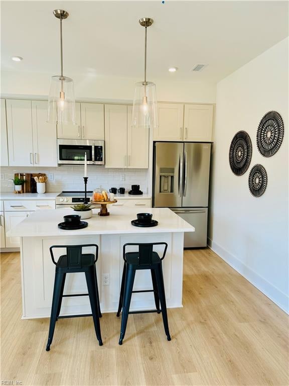 kitchen with white cabinets, stainless steel appliances, a kitchen island, and light hardwood / wood-style flooring