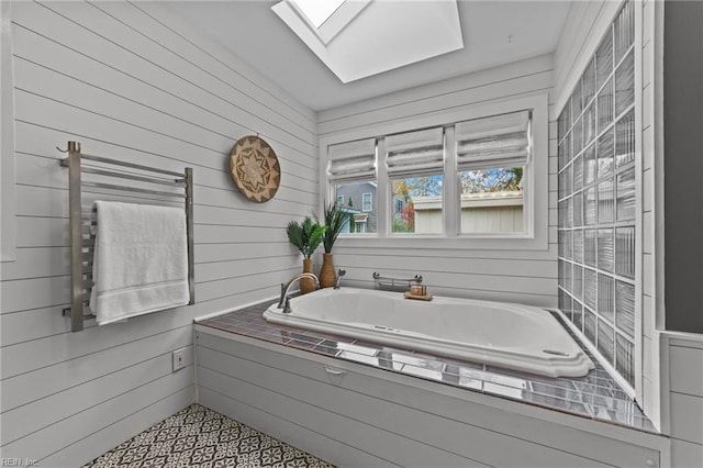 bathroom featuring a skylight, a tub, and wood walls