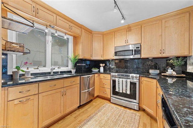 kitchen with light wood-type flooring, stainless steel appliances, dark stone countertops, and sink