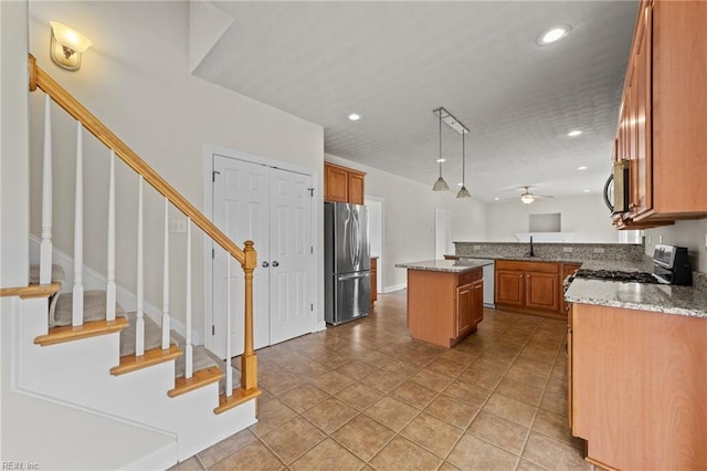 kitchen with pendant lighting, a center island, ceiling fan, light stone counters, and stainless steel appliances