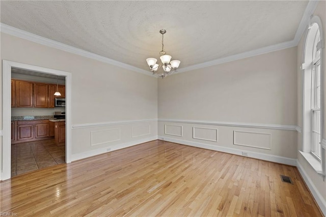 unfurnished room featuring light hardwood / wood-style flooring, a chandelier, a textured ceiling, and ornamental molding