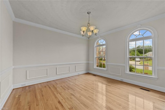 spare room with a chandelier, light wood-type flooring, a textured ceiling, and crown molding