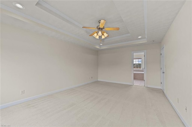 empty room with ceiling fan, a raised ceiling, light colored carpet, and ornamental molding