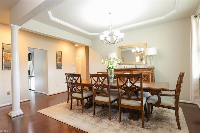 dining area featuring decorative columns, a tray ceiling, dark hardwood / wood-style floors, and a notable chandelier