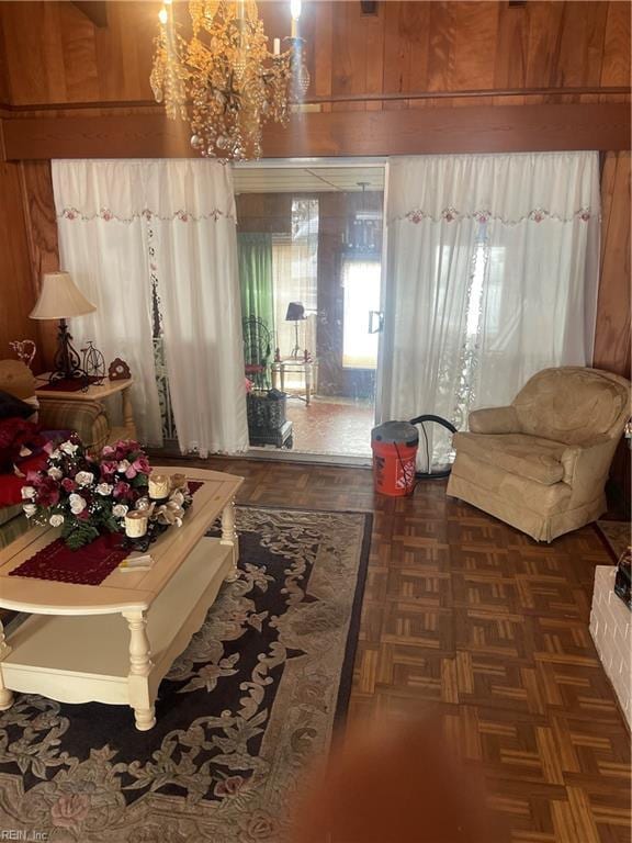 living area featuring dark parquet flooring, wooden walls, and a chandelier