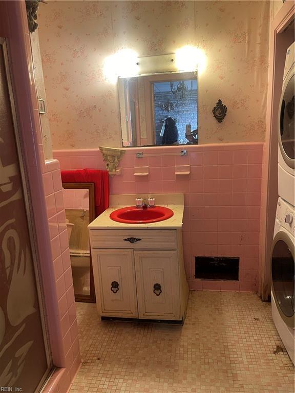 bathroom with stacked washer and dryer, vanity, tile patterned flooring, and tile walls