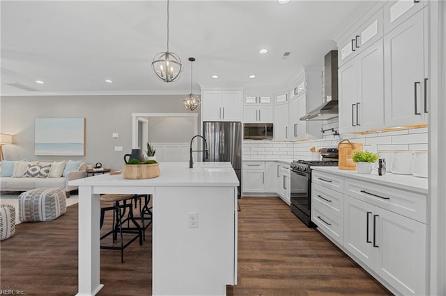 kitchen featuring white cabinets, wall chimney exhaust hood, an island with sink, decorative light fixtures, and stainless steel appliances