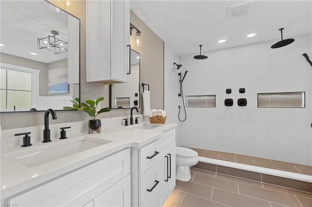 bathroom with tile patterned flooring, vanity, tiled shower, and toilet