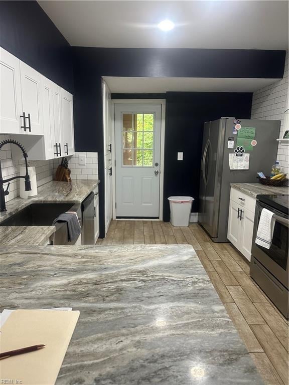 kitchen featuring decorative backsplash, stainless steel appliances, sink, light hardwood / wood-style floors, and white cabinetry