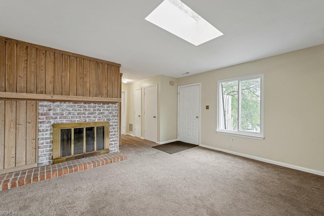 unfurnished living room with a skylight, wood walls, a fireplace, and carpet