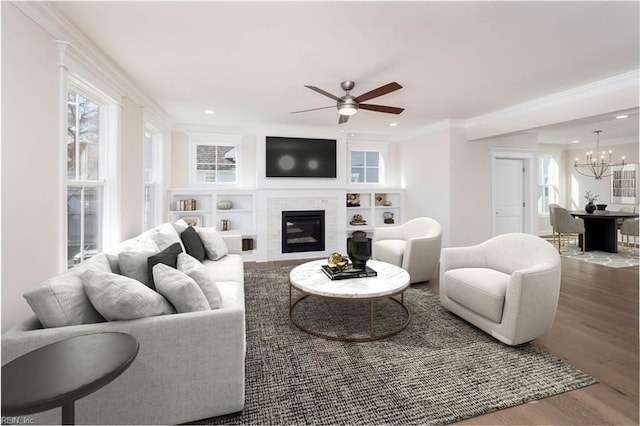 living room featuring hardwood / wood-style flooring, ceiling fan with notable chandelier, ornamental molding, and a tile fireplace